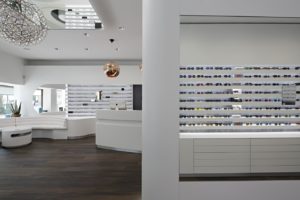 Optik Gröschner in Bruchsal Helle moderne Brillenboutique mit weißen Regalen, die zahlreiche Sonnenbrillen zeigen, und dunklem Holzboden.