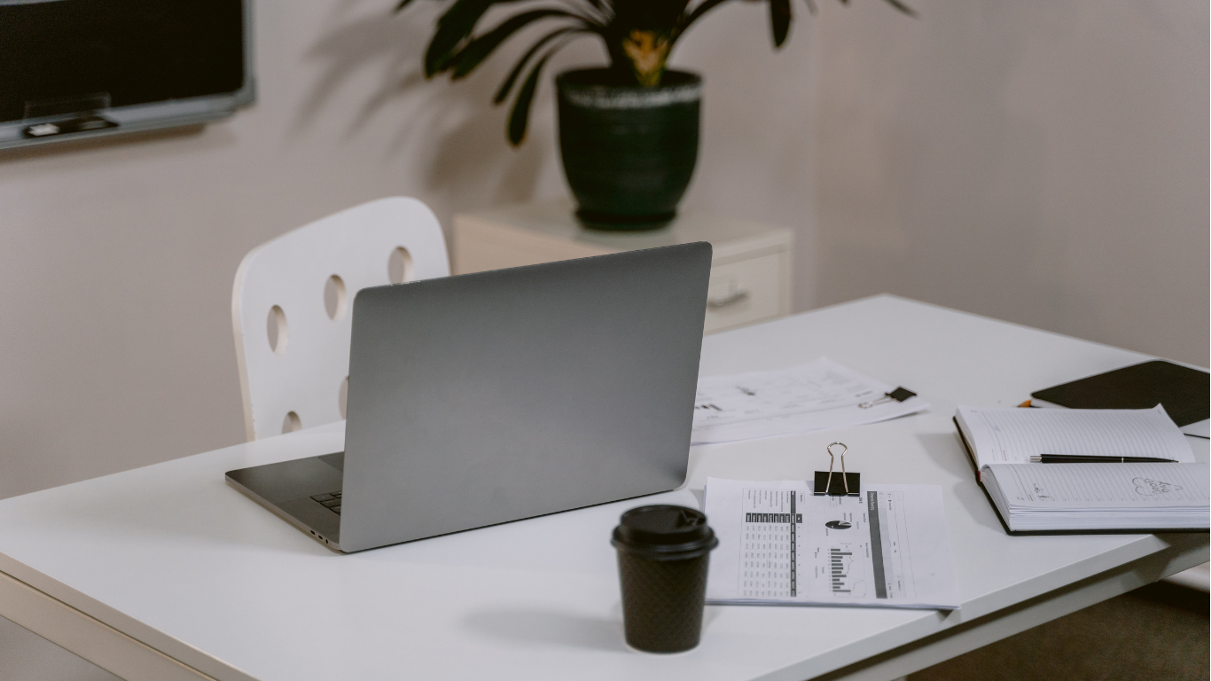 Moderner Arbeitsplatz mit aufgeklapptem Laptop, Kaffeebecher, Dokumenten und Ordnern auf weißem Tisch