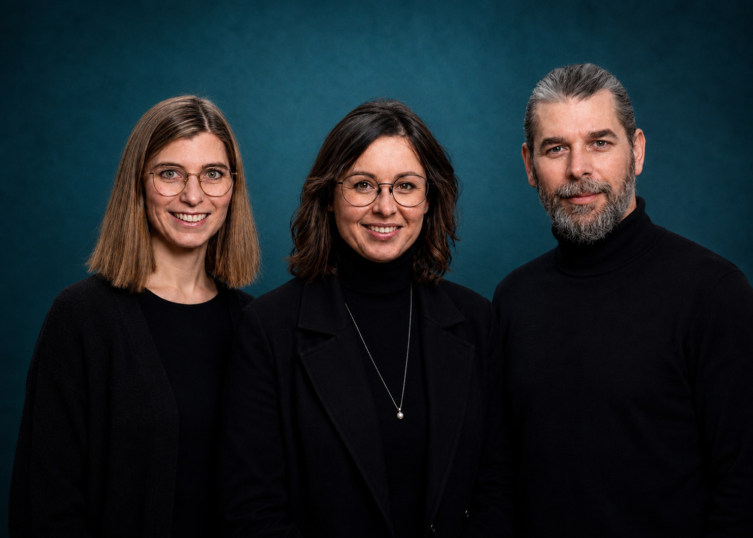 Unser Team bei Optik Gröschner Drei Personen in schwarzer Kleidung vor schwarzem Hintergrund, zwei Frauen mit Brille und ein Mann mit grauem Bart und zurückgebundenem Haar.